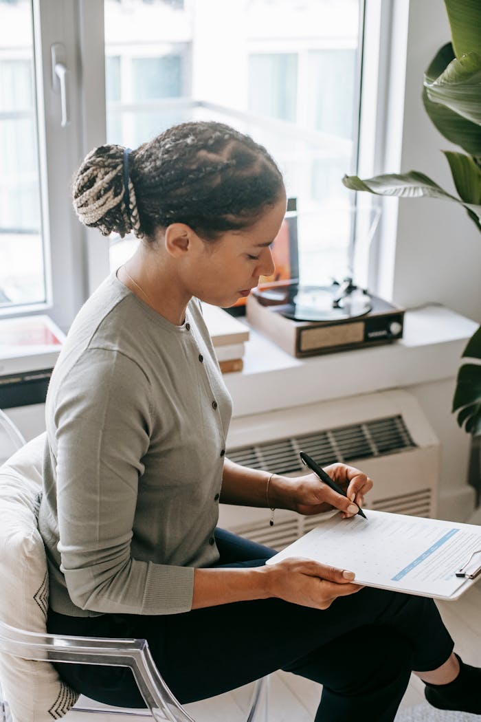Woman sitting by window writing on clipboard, possibly during a professional session.